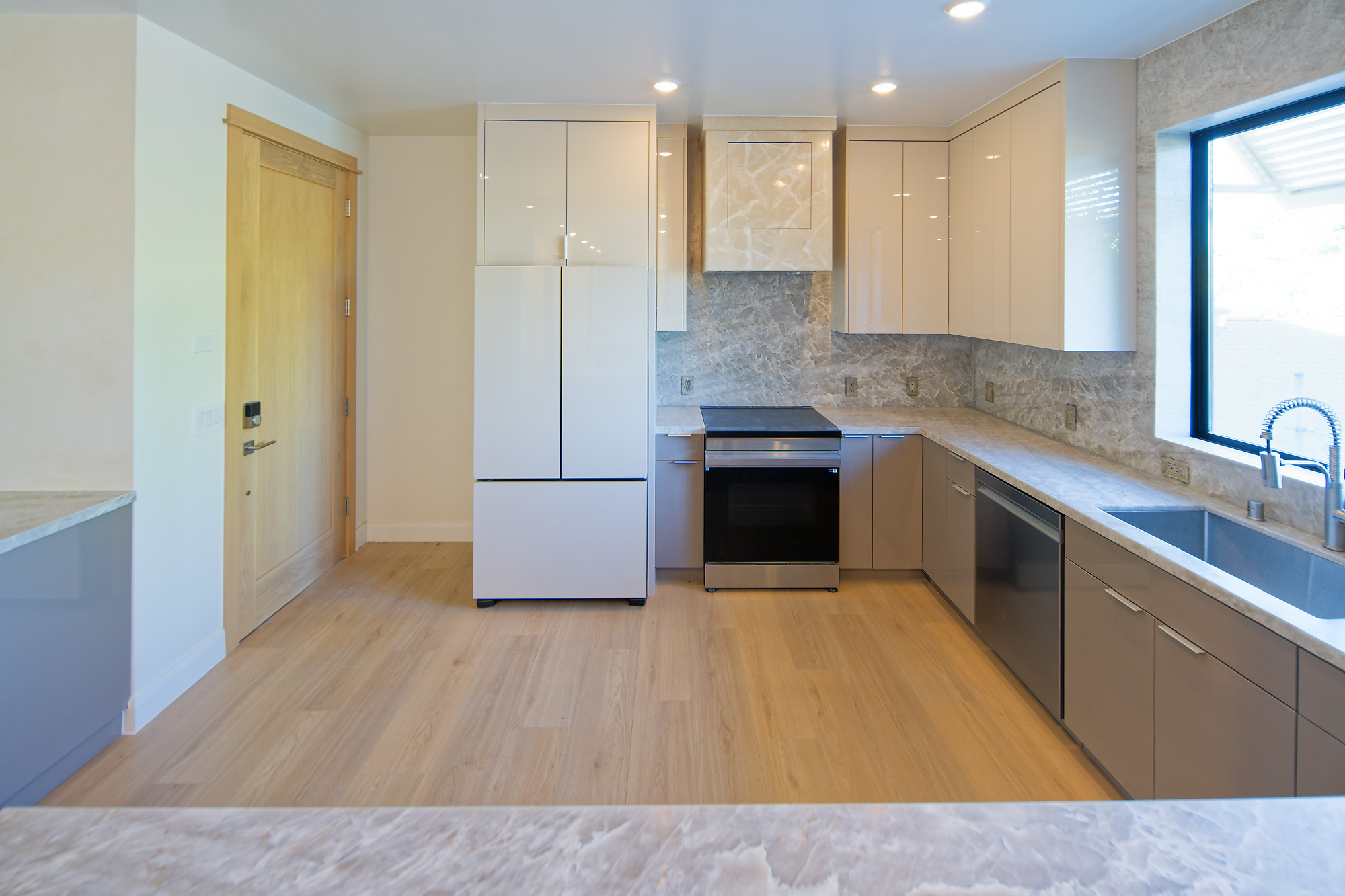 Kitchen with glossy cabinetry, stone backsplash, induction range, and a window above the sink at The Benjamin in Lake Balboa