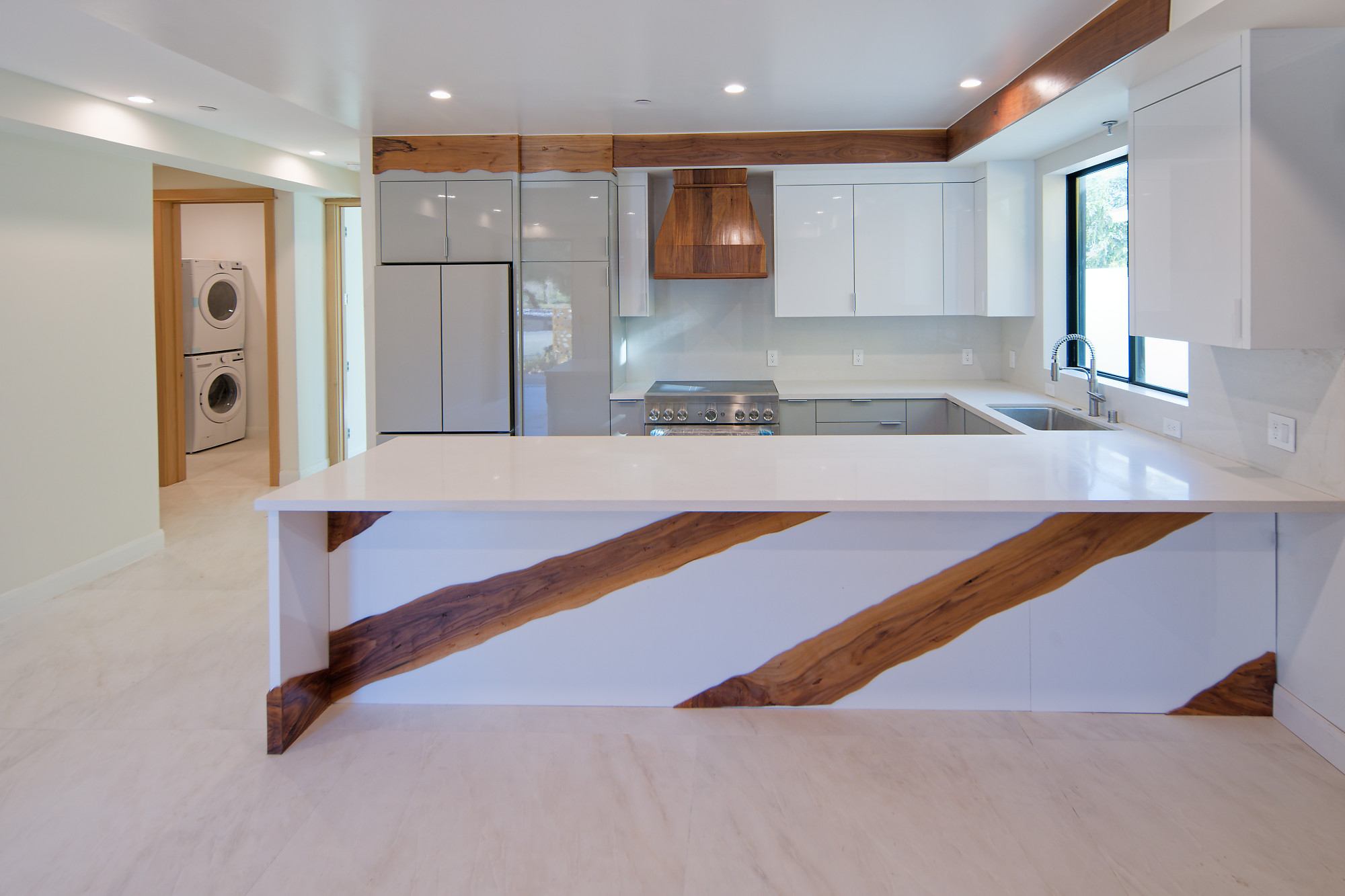 Kitchen with white cabinetry, natural wood accents, a broad peninsula, and adjacent laundry at The Benjamin in Lake Balboa