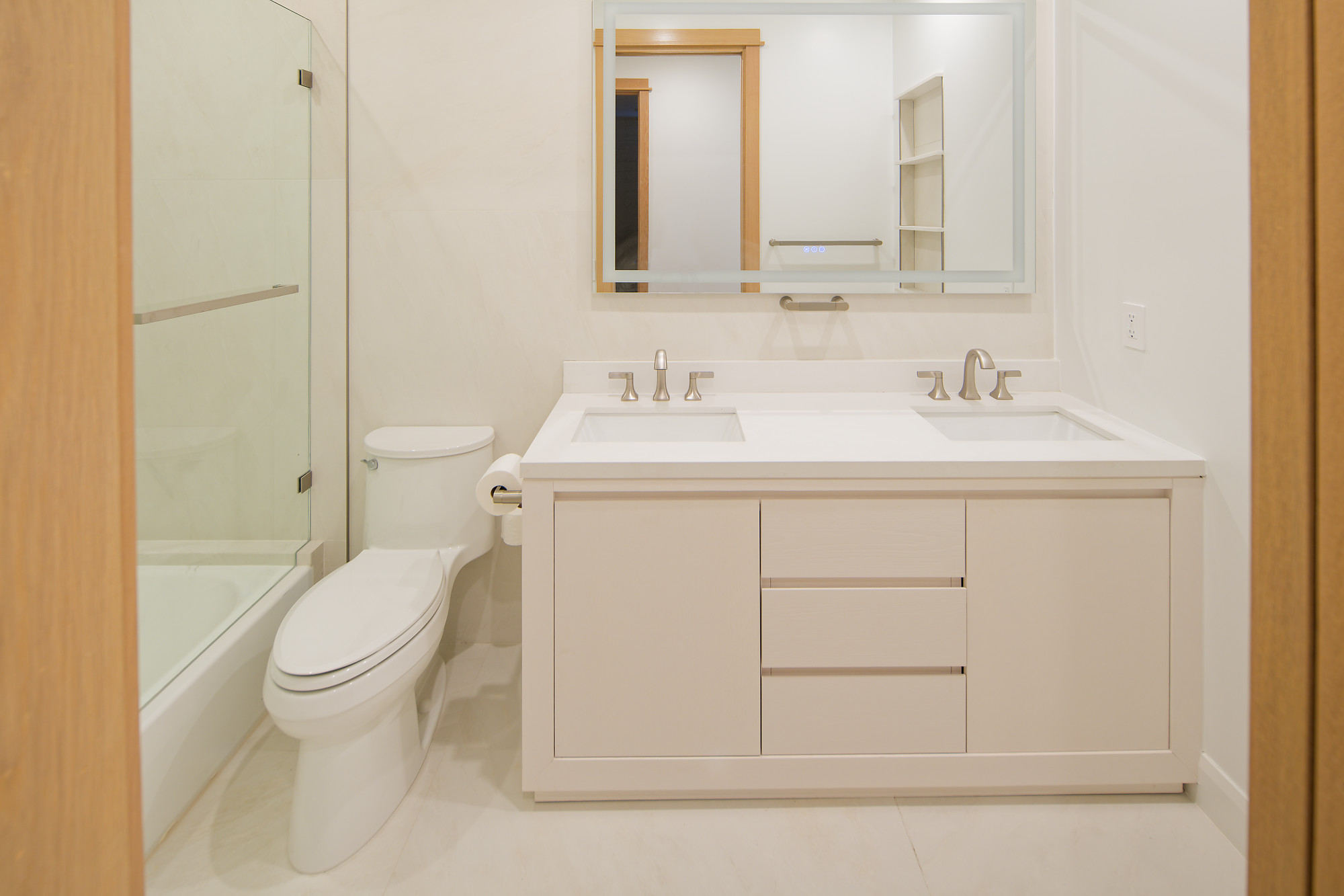 Bathroom with a double-sink vanity, illuminated mirror, and glass shower at The Benjamin in Lake Balboa